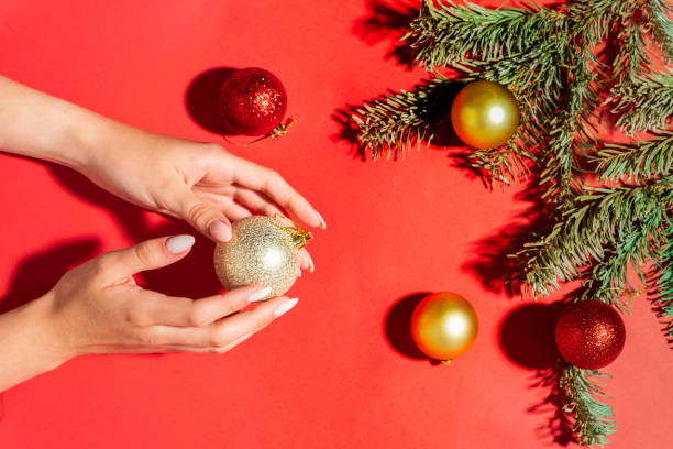 belle mani di donne su uno sfondo rosso con rami e palle dell'albero di natale, cura delle mani in inverno .. tema di capodanno di natale. - christmas fashion model human arm beautiful foto e immagini stock