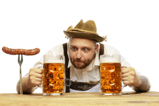 porträt eines jungen mannes in traditioneller bayerischer oder deutscher kleidung, der bierkrüge betrachtet, die über weißem hintergrund isoliert sind - wearing hot dog costume stock-fotos und bilder