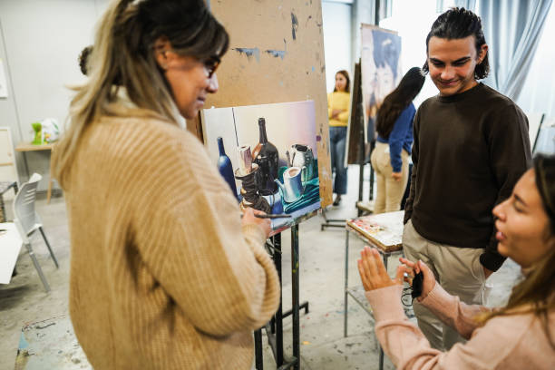 istock Mature teacher working with art students during painting class at school - Focus on canvas painting 1418153024