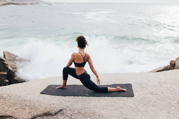 istock Young woman practicing yoga on mat by ocean at evening 1418164797
