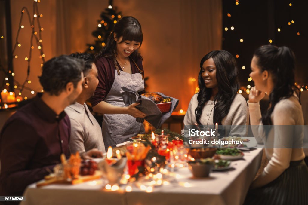 happy friends having christmas dinner at home holidays and celebration concept - multiethnic group of happy friends having christmas dinner at home Dinner Party Stock Photo