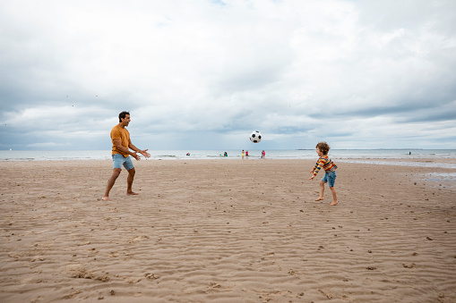 A shot of a mid adult father and his young boy playing with a football on the sand at a beach in Seahouses, Northumberland. They are having a fun time together, the young boy is throwing the ball to his father.