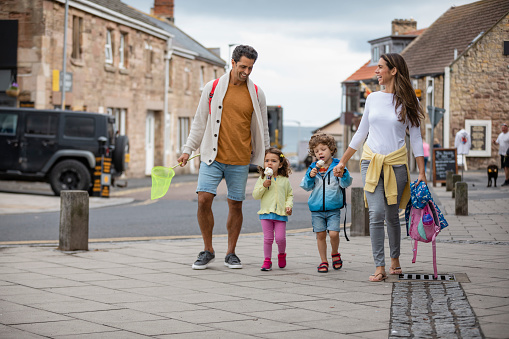 A shot of a Hispanic family walking along a street in Seahouses, Northumberland. The children are enjoying ice creams, they are ready to go to the beach.