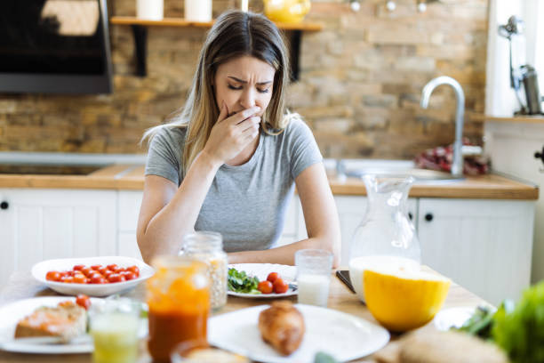 Woman feeling sick during breakfast time in dinning room Young woman feeling nausea during breakfast time at dining table nausea photos stock pictures, royalty-free photos & images