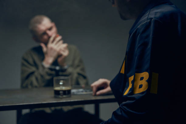 un'immagine sfocata di un prigioniero fumatore con una sigaretta durante l'interrogatorio, è seduto a un tavolo in caratteri di un agente dell'fbi in una stanza buia - catturare unimmagine foto e immagini stock