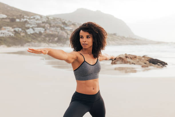 istock Female in sportswear practicing Warrior pose while standing on beach at sunset 1418178349