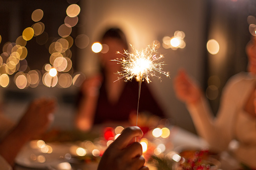 holidays and celebration concept - close up of hand with burning sparkler at christmas dinner party