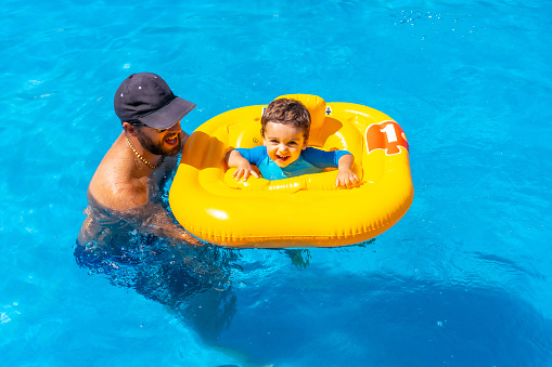 Father playing with his son with a yellow float in the pool in summer
