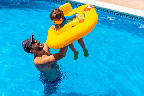 istock Father playing with his son with a yellow float in the pool in summer 1418179546