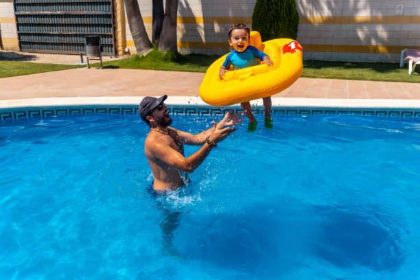 istock Father playing with his son with a yellow float in the pool in summer, throwing it 1418179582