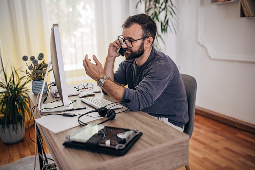 Man working on computer at home office and talking on the smart phone