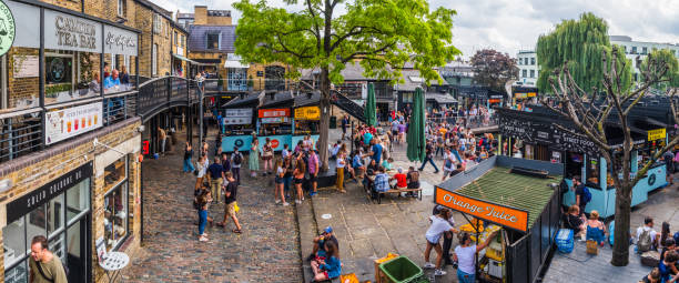 London Camden Market crowds of people at food stalls panorama Crowds of shoppers and tourists in the courtyards of Camden Market beside the street food stalls in London, UK. camden lock stock pictures, royalty-free photos & images