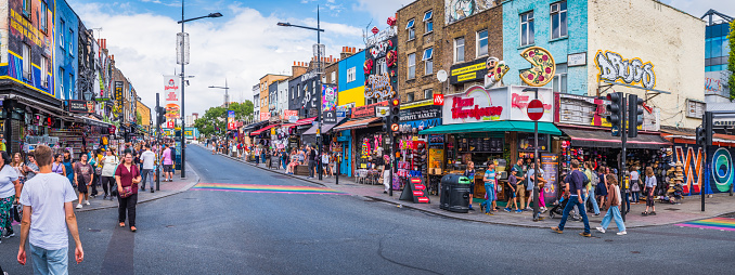 Crowds of tourists and shoppers on Camden High Street beside the colourful fashion and food stores in the heart of London, UK.