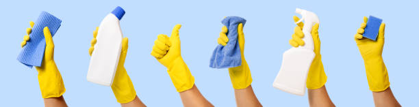 mano con guanto di gomma gialla che tiene i prodotti per la pulizia su sfondo blu. striscione - kitchen glove foto e immagini stock