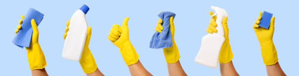 mão com luva de borracha amarela segurando materiais de limpeza em fundo azul. estandarte - kitchen glove - fotografias e filmes do acervo