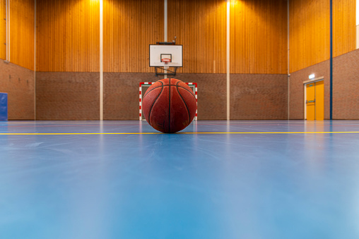 Interior of school gym with blue flooring  and one basketball.