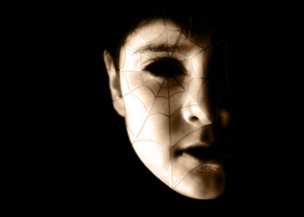 sepia toned horrifying portrait of a spotlit child, boy with spooky make up and blank hollow ghost like eyes, spot light over face covered with spider web or cobweb scars over black halloween backgrounds - facial expression child asia asian and indian ethnicities imagens e fotografias de stock