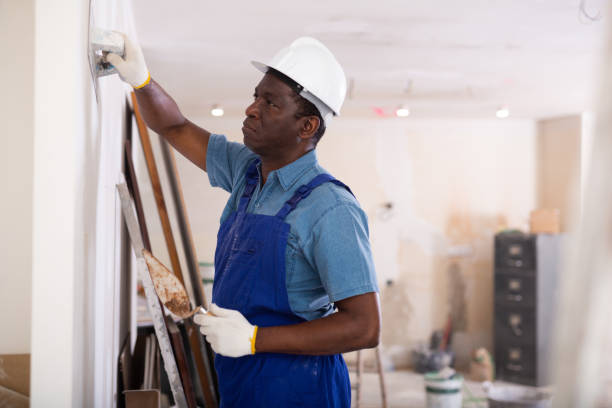 istock Painter in blue overalls leveling plaster on the wall with spatula 1418190313