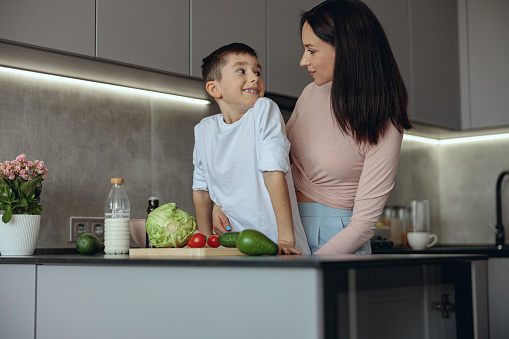 Portrait shot pf beautiful mother and little con looking at each other in kitchen. Cooking concept.