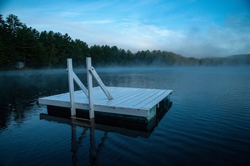 A calm scene of a mist covered lake with a white wooden dock in the evening