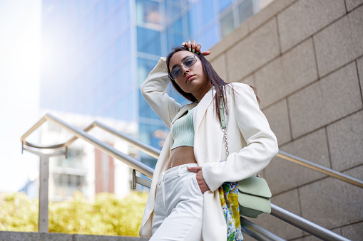 Woman in white suit standing on stairs on background of modern buildings. High quality photo