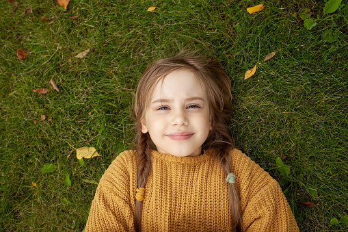 Young girl in yellow sweater on green grass background, top view