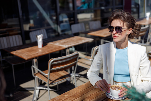 Attractive business woman in sunglasses drinking coffee sitting in cafe and looking away