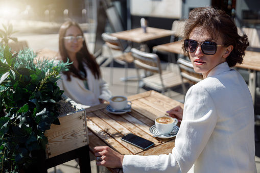 Attractive business woman in sunglasses drinking coffee sitting in cafe and looking away