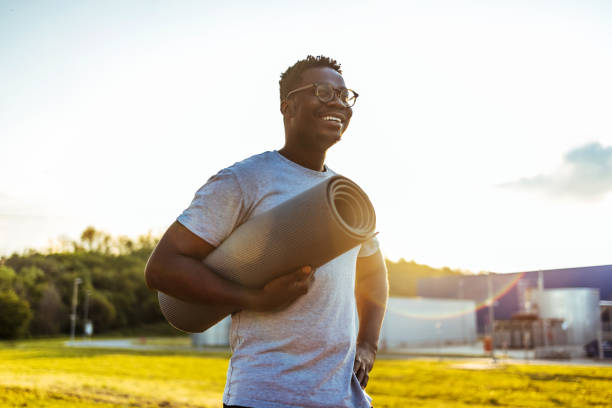화창한 날에 요가 매트를 들고 웃고있는 아프리카 계 미국인 남자. - men exercising equipment relaxation exercise 뉴스 사진 이미지