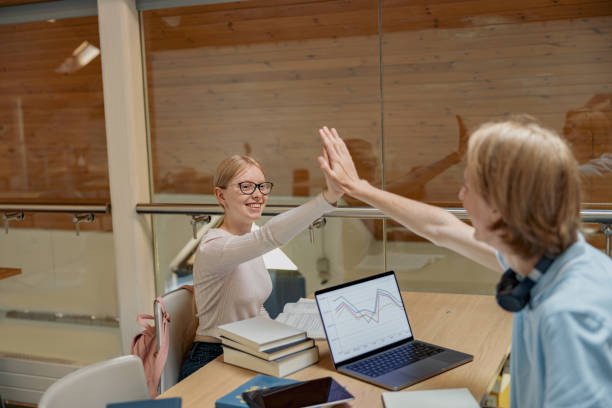 istock Two happy friends students clap hands after finishing work on project sit in university library 1418197907