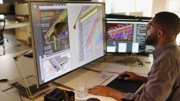 CAD home insulation Stock Photograph of an African American / Afro-Caribbean male working with large computer screens & compute Aided design. He’s designing built in insulation structures in domestic homes . architecture project stock pictures, royalty-free photos & images