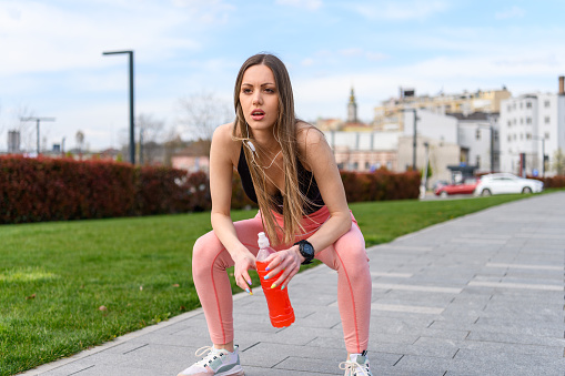 Young Attractive Woman is Taking a Break After an Exercise while Listening to Music, and Drink Refreshing Drink.