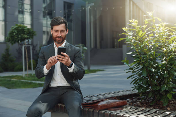 istock Smiling office worker have a rest during break outside office and scrolling social media on phone 1418211154