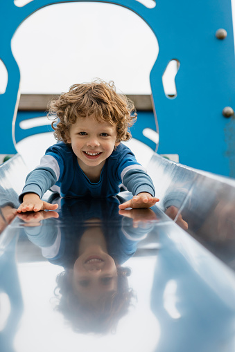 A close up front view of a young boy having loads of fun and being brave sliding down a slide in a playground head first in a public park in Seahouses in the North East of England he is smiling and looking into the camera.