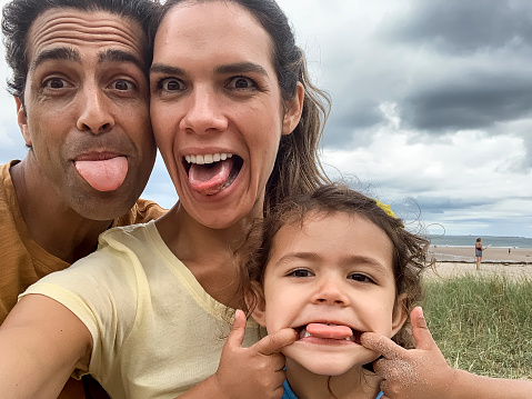A close up selfie of three family members pulling faces and looking into the camera for a silly selfie on their trip to the beach in Seahouses in the North east of England