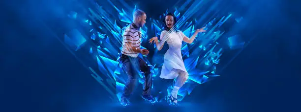 Photo of Cheerful, stylish young couple dancing rock-and -roll, lindy hop over dark background with neon fluid elements. Art, beauty, dance concept
