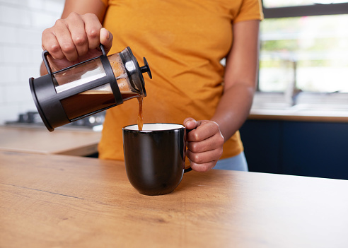 A close up of a young woman pouring French press coffee into a mug in the kitchen. High quality photo