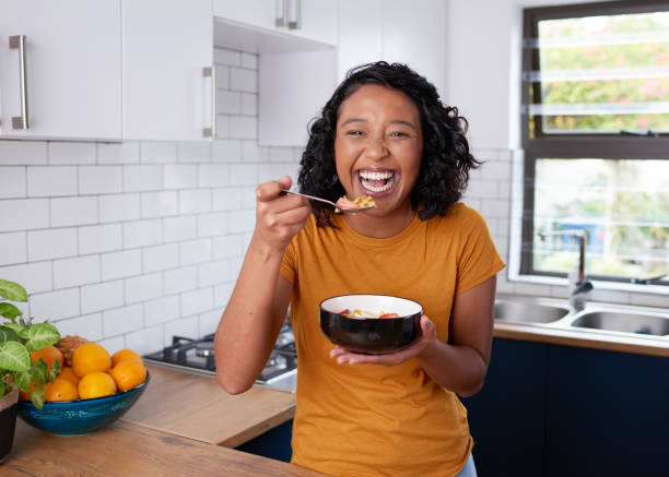 istock A young woman laughs while eating breakfast cereal in the kitchen 1418212674