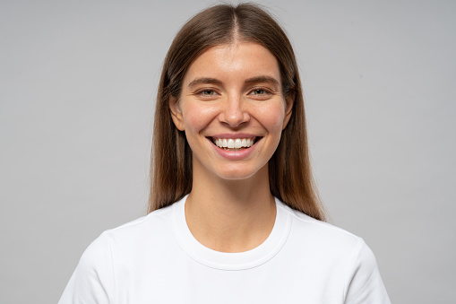 Positive human emotions. Headshot of happy emotional teenage girl in white t-shirt looking at camera with perfect candid toothy smile laughing on gray studio background, having fun