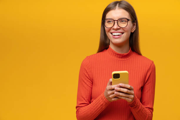 Smiling woman having fun browsing social media network on phone on yellow copy space background Smiling young woman in glasses and red clothes having fun browsing social media network on her smartphone, reading funny posts, memes, chatting in comments on yellow background with copy space i see you meme stock pictures, royalty-free photos & images