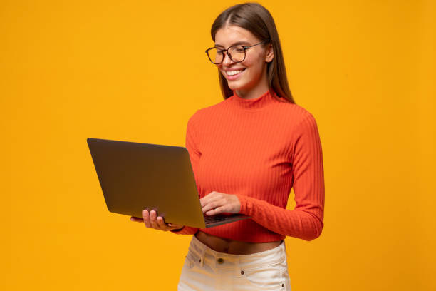 Portrait of intelligent woman teacher having lesson online on laptop, isolated on yellow background Side view portrait of attractive intelligent smart female teacher in glasses and red turtleneck having lesson online on laptop isolated on yellow background. Remote education high collar stock pictures, royalty-free photos & images