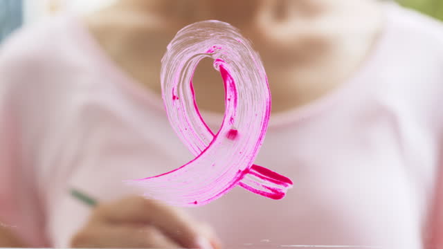 Woman draw pink ribbon sign on mirror, sign of October Breast Cancer Awareness month