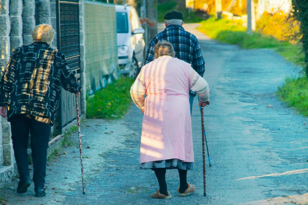 Santiago de Compostela, Spain- December 15, 2021: Rear view of two senior women walking slowly with walking canes along the road , senior man in the background, empty street view.