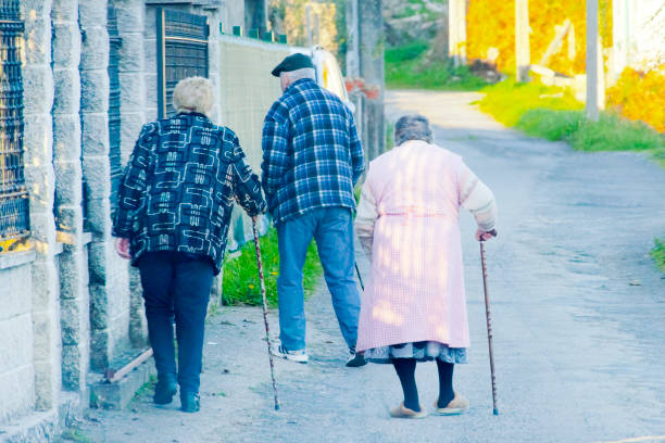 Santiago de Compostela, Spain- December 15, 2021: Rear view of three senior people walking slowly with walking canes along the road , empty street view in the background.