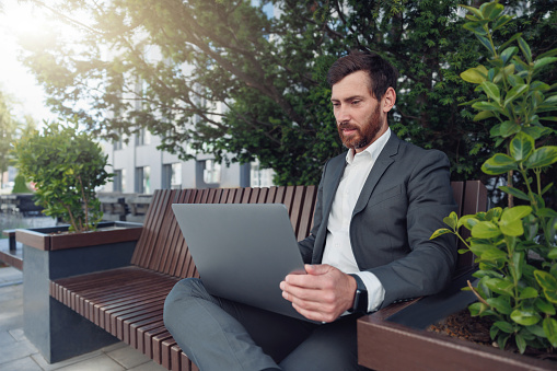 Business man office worker working on urban park background using laptop. Blurred background