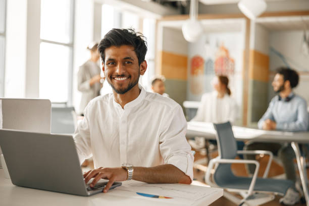 istock Smiling Businessman working laptop while sitting in modern office on colleagues background 1418217436