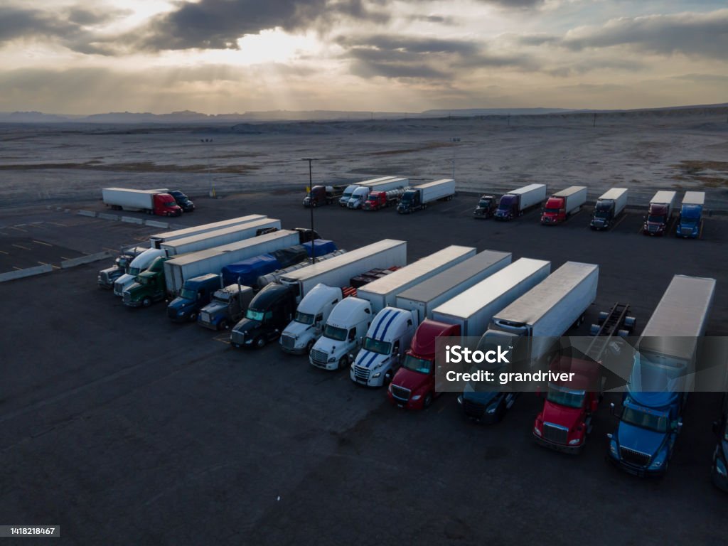 Semi Truck Lorries Lined Up for the Evening in a Large Parking Lot at a Truck Stop in the Desert Area of Eastern Utah on I-70 At Dusk Under a Dramatic Cloudscape Sunset Sky Convoy Stock Photo