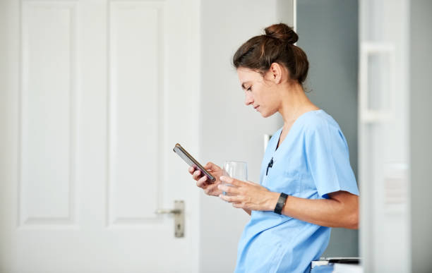 junge krankenschwester mit einem glas wasser mit handy im krankenhaus - female nurse nurse scrubs female doctor stock-fotos und bilder