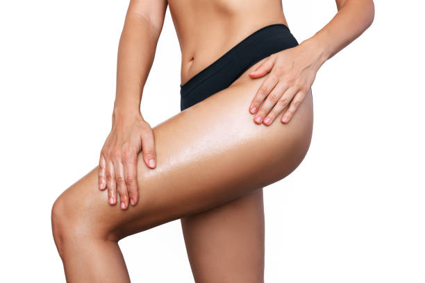 Young woman smearing her thigh with cosmetic oil. The girl moisturizes the skin after sunburn Cropped shot of young slender tanned woman smearing her thigh with cosmetic oil isolated on a white background. Cosmetology, massage, spa products. The girl moisturizes the skin after sunburn hand thigh stock pictures, royalty-free photos & images