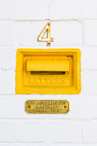 Brass house number, bright yellow letter box and brass 'no advertising material' sign on white painted brick wall